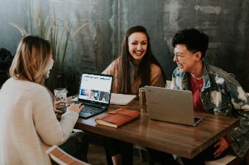 Three students sitting at a large table studying with their laptops 