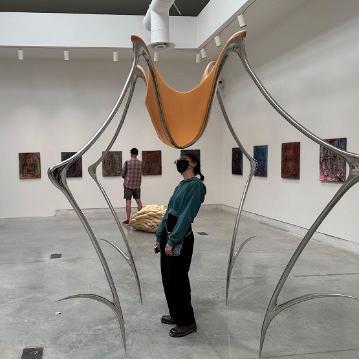Two people viewing sculptures and paintings in an art gallery.