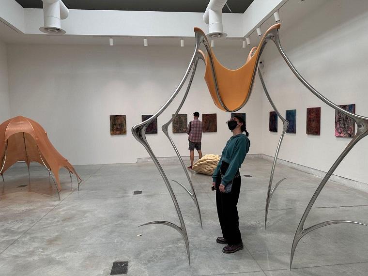 A person standing in an art gallery with sculptures and framed artworks.