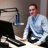 Man in a studio sitting by a microphone and computer.