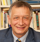 Man in suit smiling in front of a bookshelf.