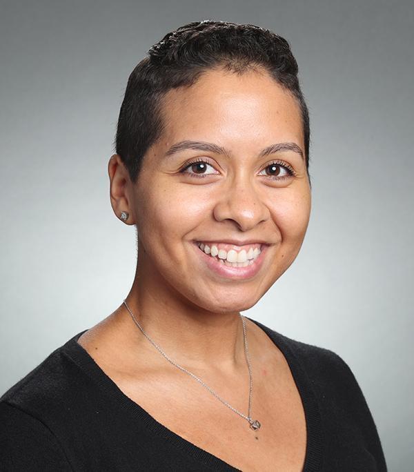 Woman smiling, wearing a black shirt, grey background.