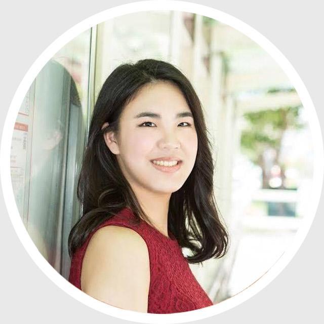 A person smiling, standing outdoors against a wall.