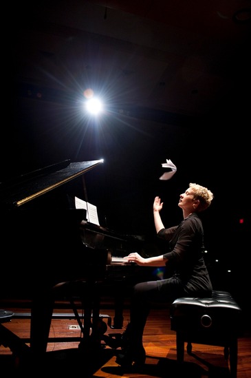 Pianist Teresa McCollough playing a concert grand with her right hand extended up, knocking the sheet music off the music desk and dramatically into the air