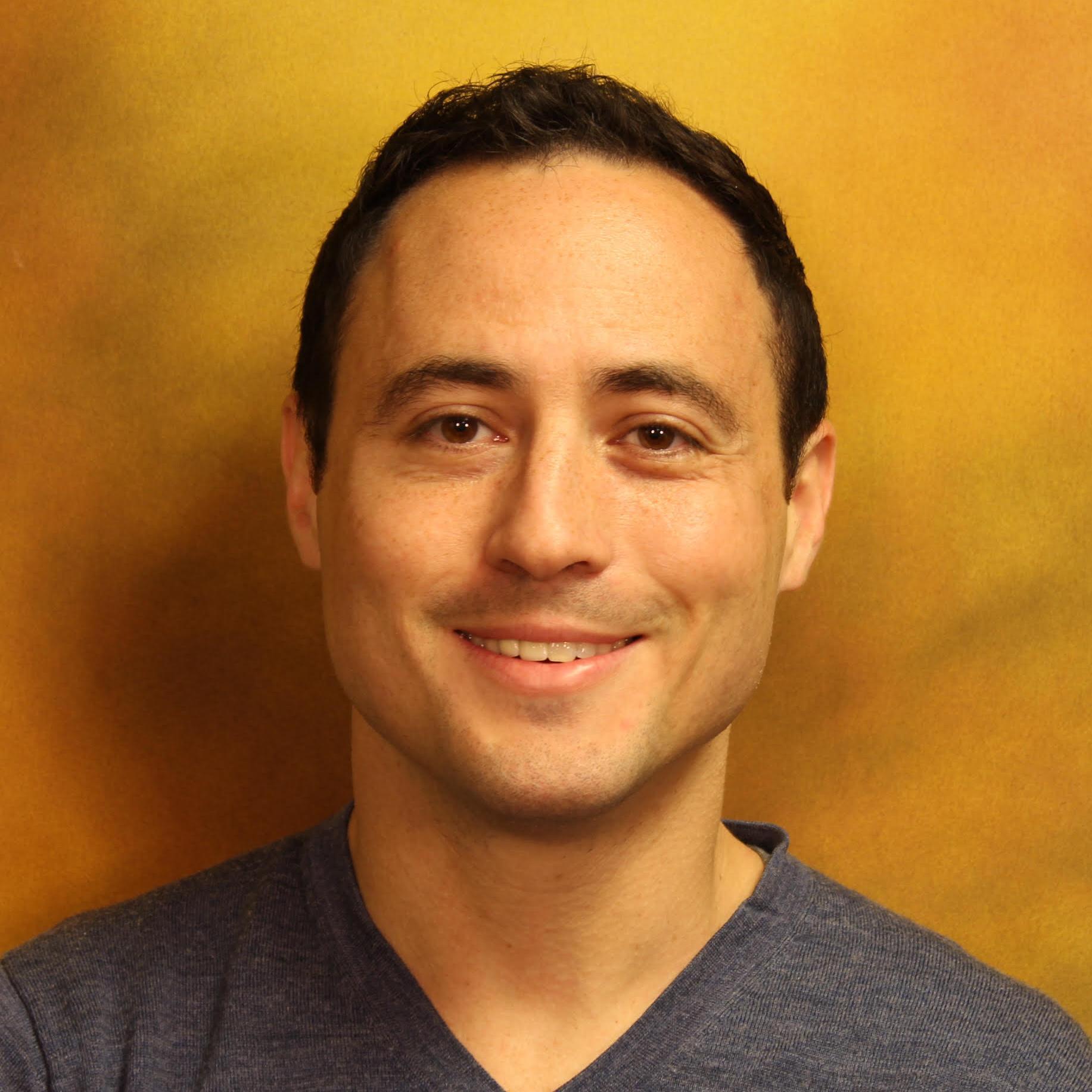 A person smiling against a yellow-orange background.