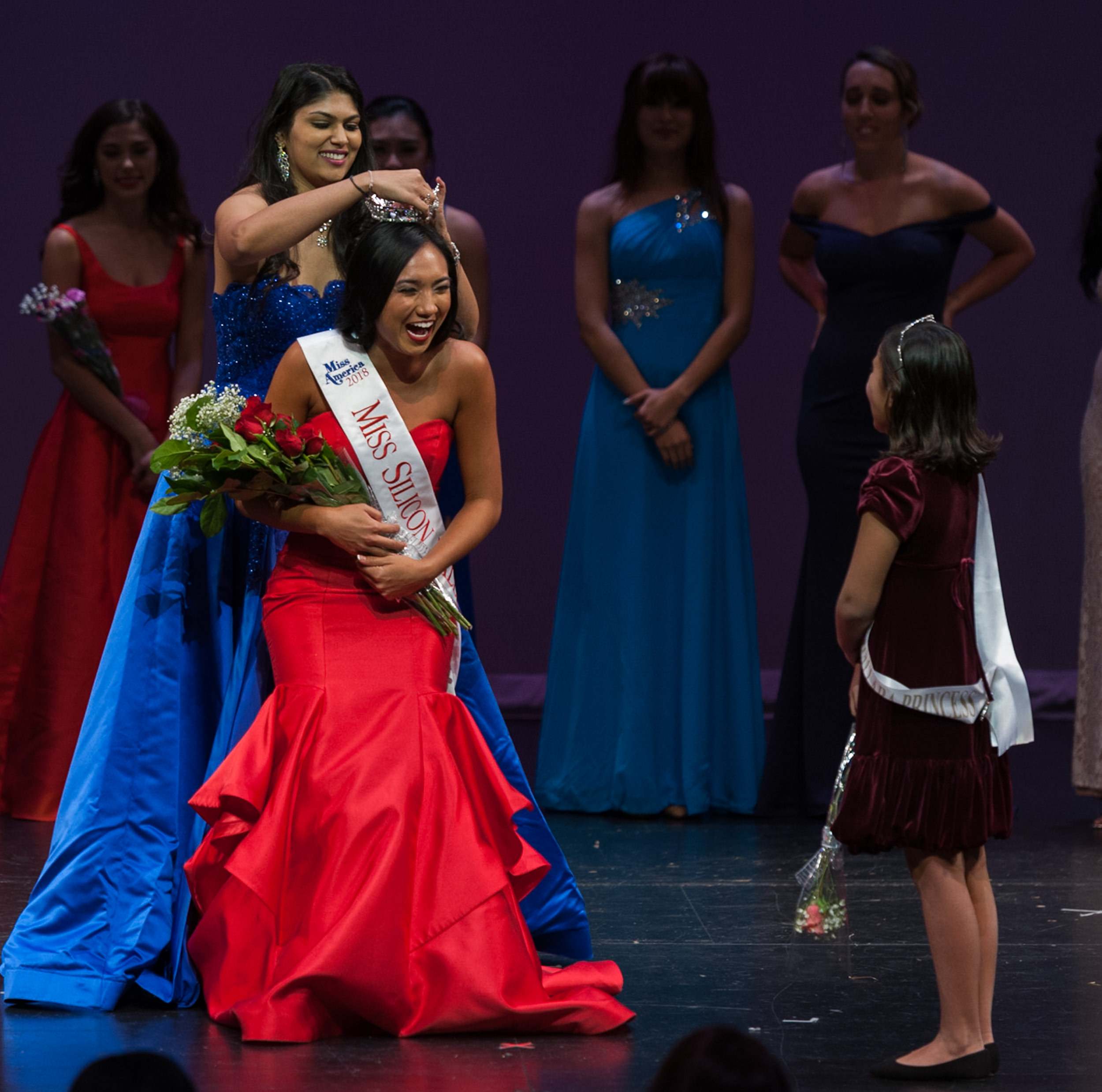 A pageant winner is crowned on stage with a bouquet and sash.