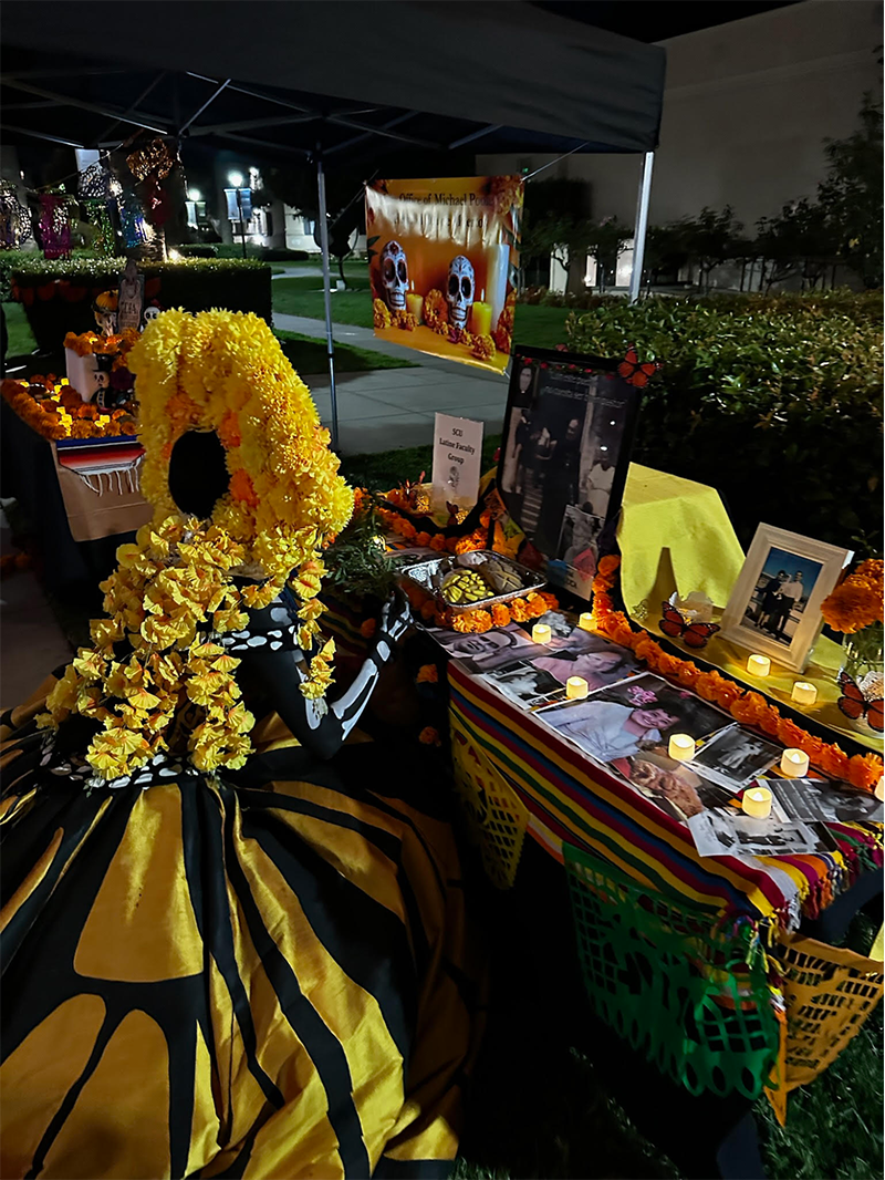Woman dressed in yellow and black viewing a table dedicated to loved ones for day of the dead