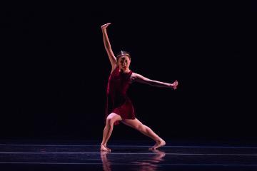 A dancer in a dynamic pose on a dark stage. 