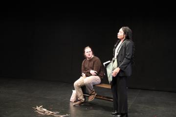 A man sitting on a bench looking up at a woman in a black suit standing