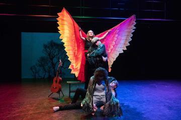 Two performers on stage, one with colorful, illuminated wings.