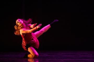 Female dancer in a red dress kneeling with one leg and both arms outstretched