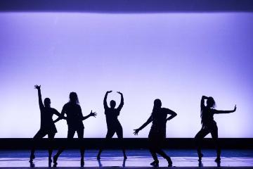 Silhouettes of five people dancing on a stage with purple lighting.