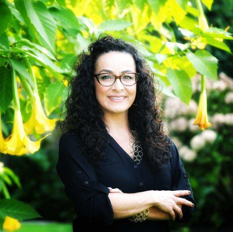 A woman wearing glasses standing in front of yellow flowers.
