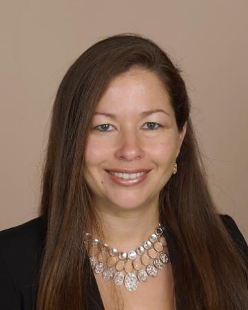 A woman smiling, wearing a necklace and a black top against a beige background.