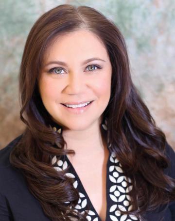 A smiling person with long hair wearing a dark blazer and patterned top.