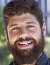 A man with a beard smiling outdoors.