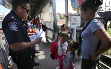 A United States Customs and Border Protection Officer checks the documents of migrants, before being taken to apply for asylum in the United States, on the International Bridge 1 in Nuevo Laredo, Mexico, Wednesday, July 17, 2019. (AP Photo/Marco Ugarte)