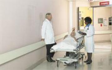 Two medical professionals talking in a hallway over a patient laying on a gurney between them. 