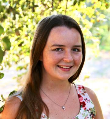 A smiling woman outdoors with trees in the background.