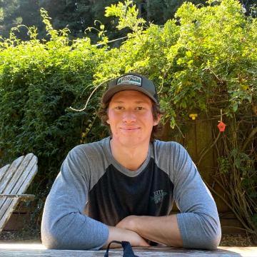 A person sits at a table outdoors under a green umbrella.