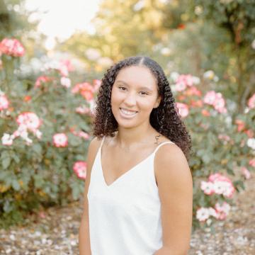 A person sitting outdoors among flowers, smiling for the camera.