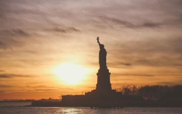 Sunset view of the Statue of Liberty silhouetted against the sky.