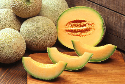 Alt text: Fresh cantaloupe slices and whole cantaloupes on a wooden surface.