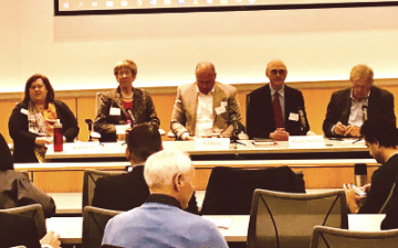 A panel discussion at Santa Clara University January 2020. Five panelists sitting at a table and audience members in rows of auditorium style chairs. 