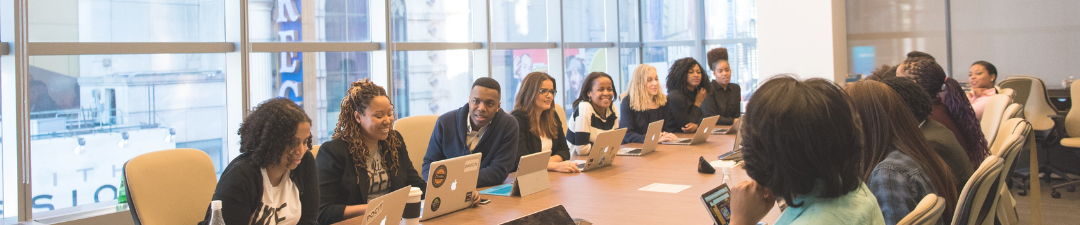 A business meeting with diverse group of participants sitting at a conference table with laptops and notebooks engaging in a conversation