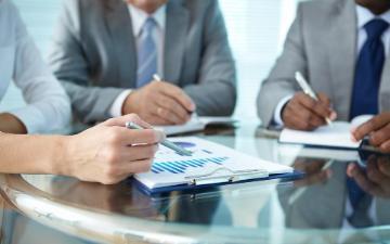 Three people sitting around a conference table looking at business proposals.