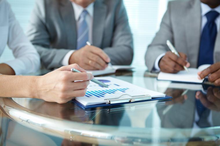 Three people sitting around a conference table looking at business proposals.