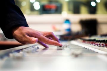 Hand adjusting audio mixer in a recording studio.