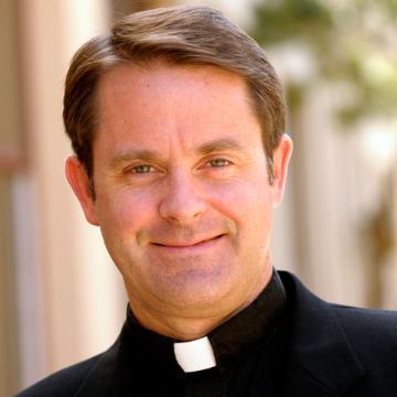 A man in a clerical collar smiling.