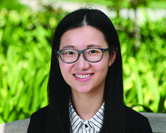 A person with glasses in front of green foliage.