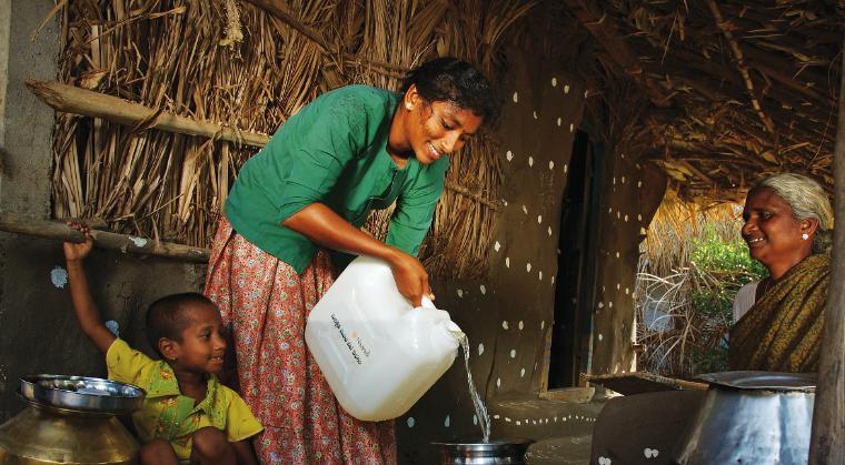 A person pouring water from a white container into a metal container.
