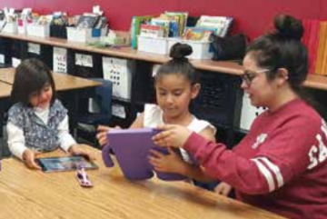 An adult and two children at a table using tablets.