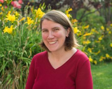 A person in a red sweater smiling in a garden.