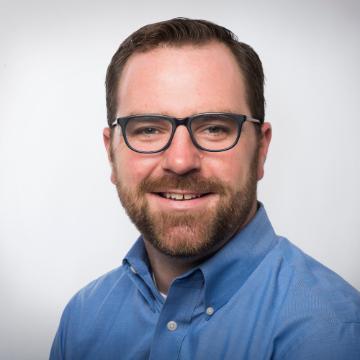 A person in glasses and a blue shirt smiling.