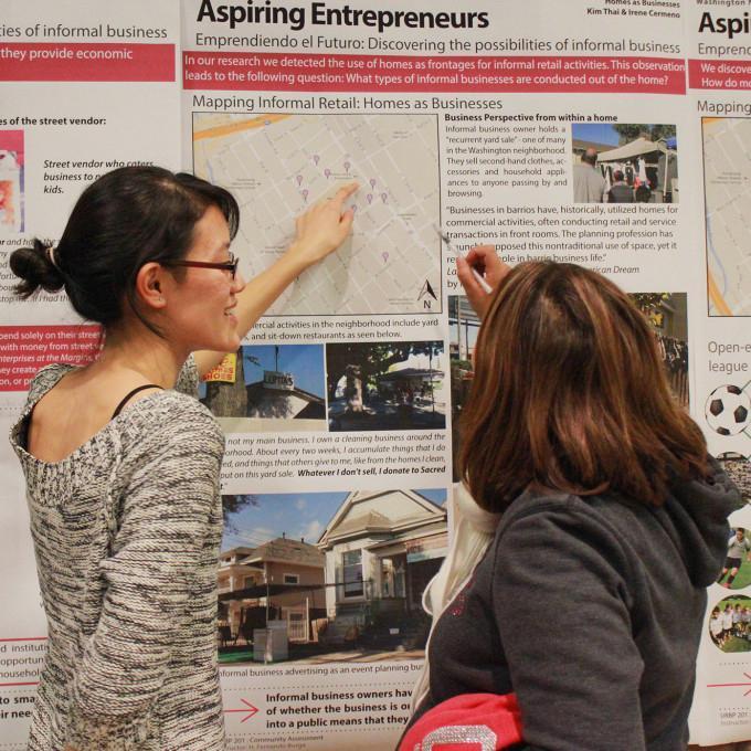 Two women discussing a wall display titled 