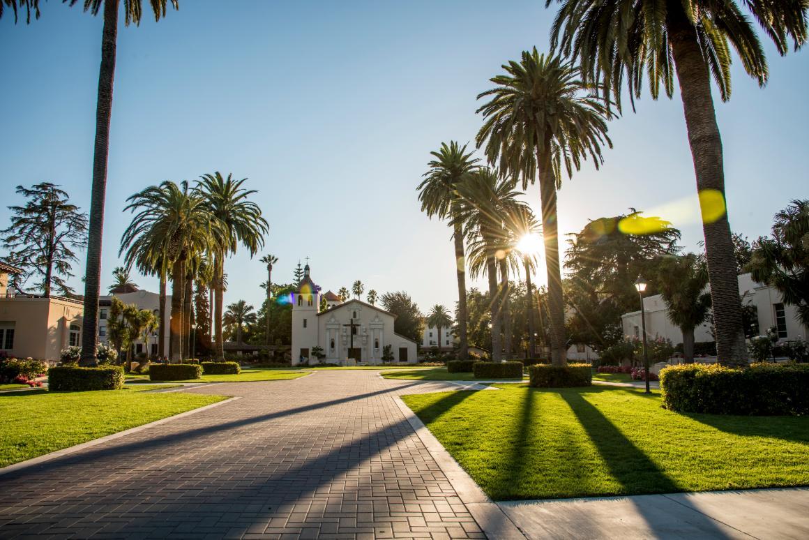 A road lined with palm trees leading to a mission-style building.