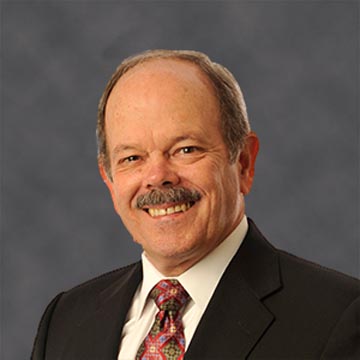 Man in a suit smiling, with a grey background.