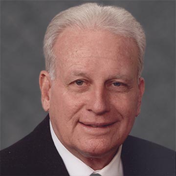 Portrait of Stephen C. Schott in a suit against a grey background.
