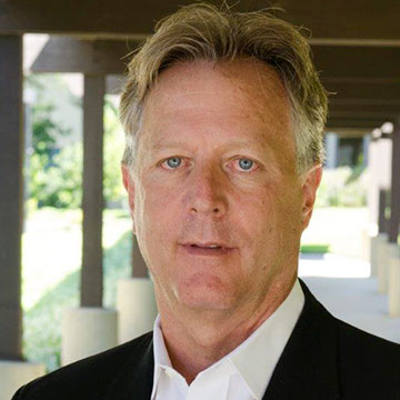 A man wearing a suit under a shaded outdoor area.