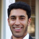 A man smiling, wearing a white shirt and dark blazer.
