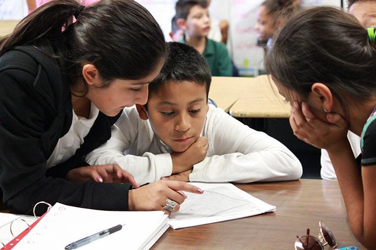 A teacher helps a student with schoolwork at a desk.