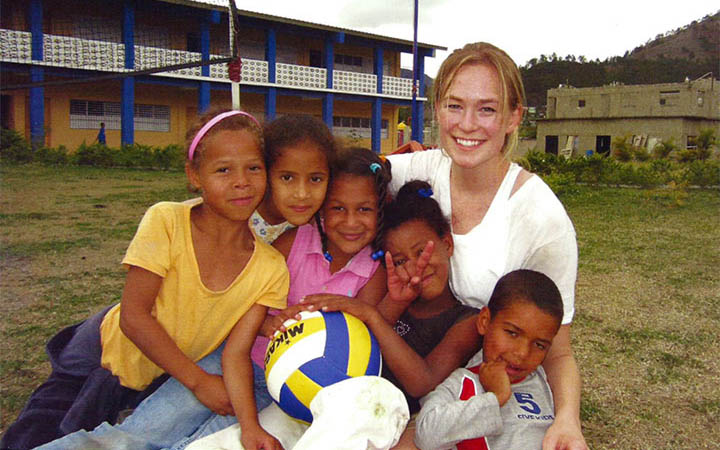 A person surrounded by smiling children holding a soccer ball.