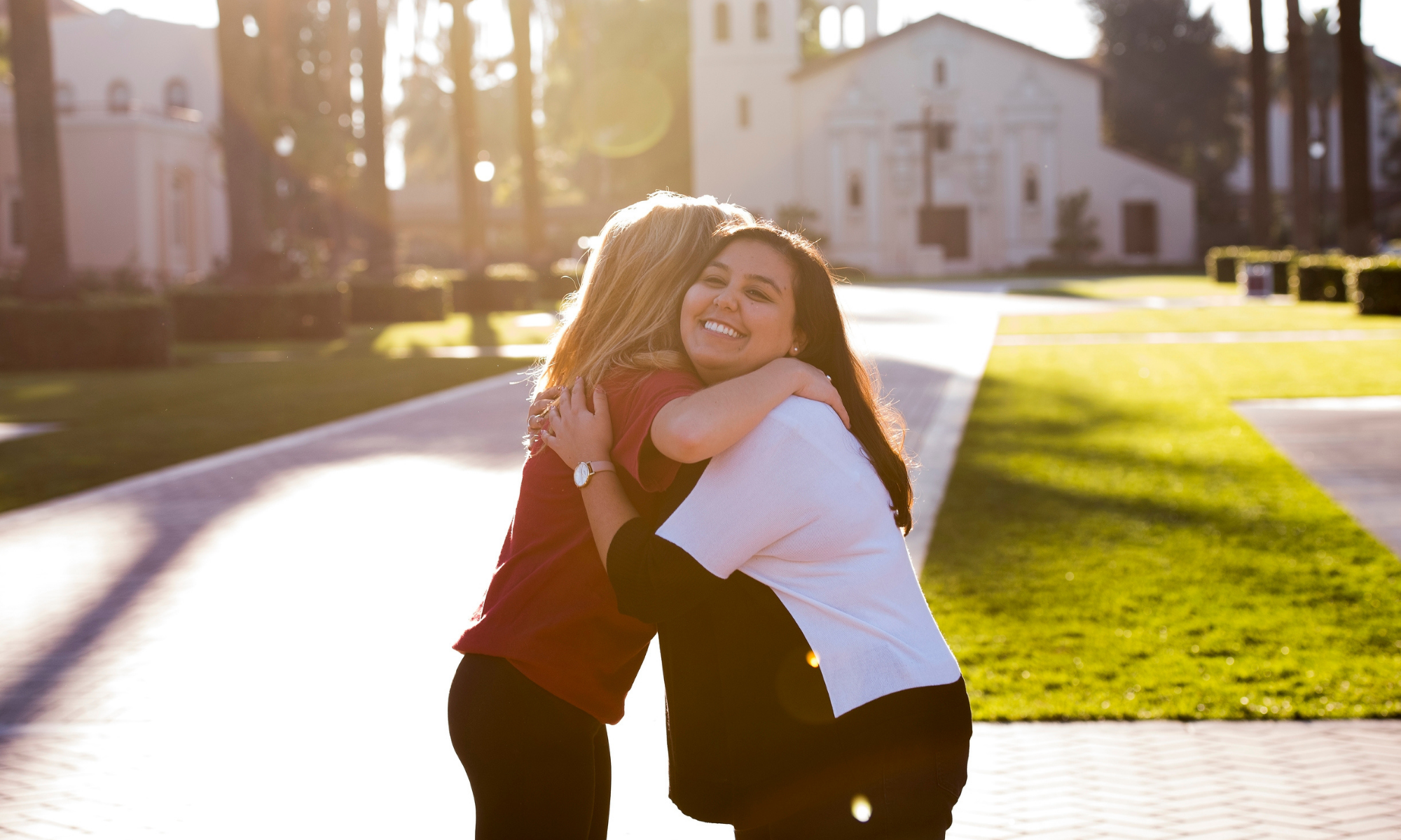 Two people hugging on a sunny pathway at a park.