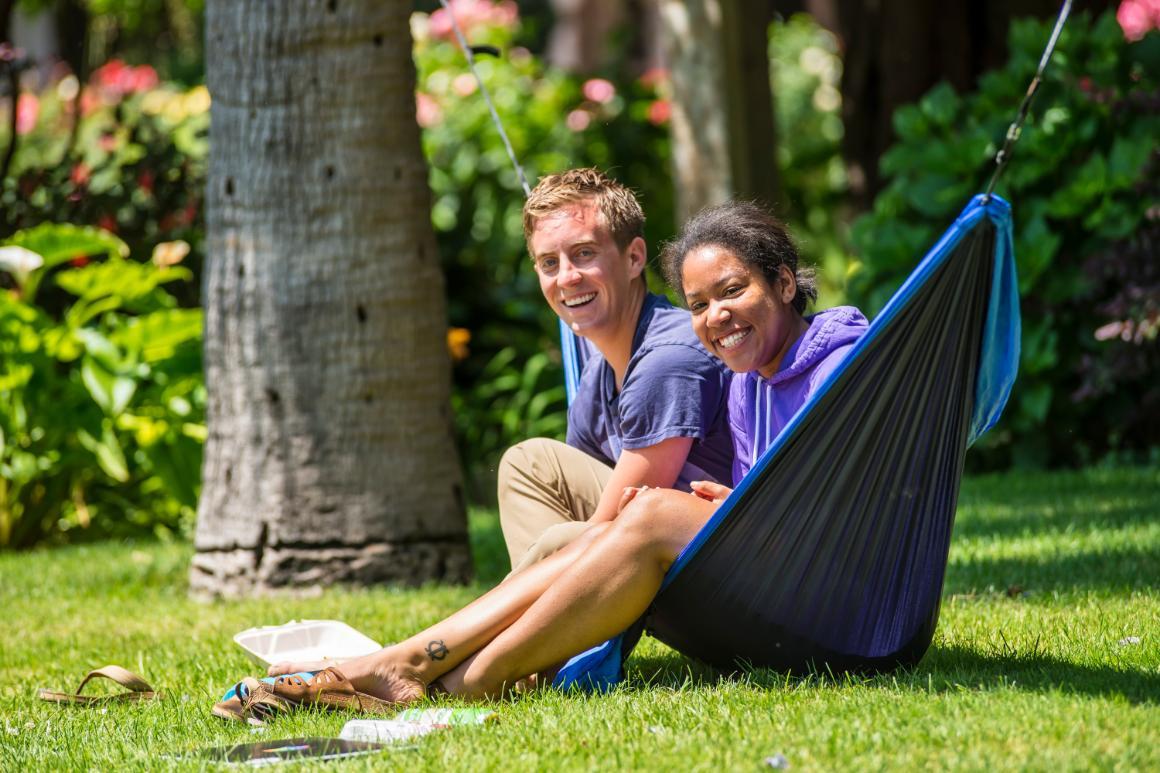 Two people relaxing on a hammock outdoors on a sunny day. 