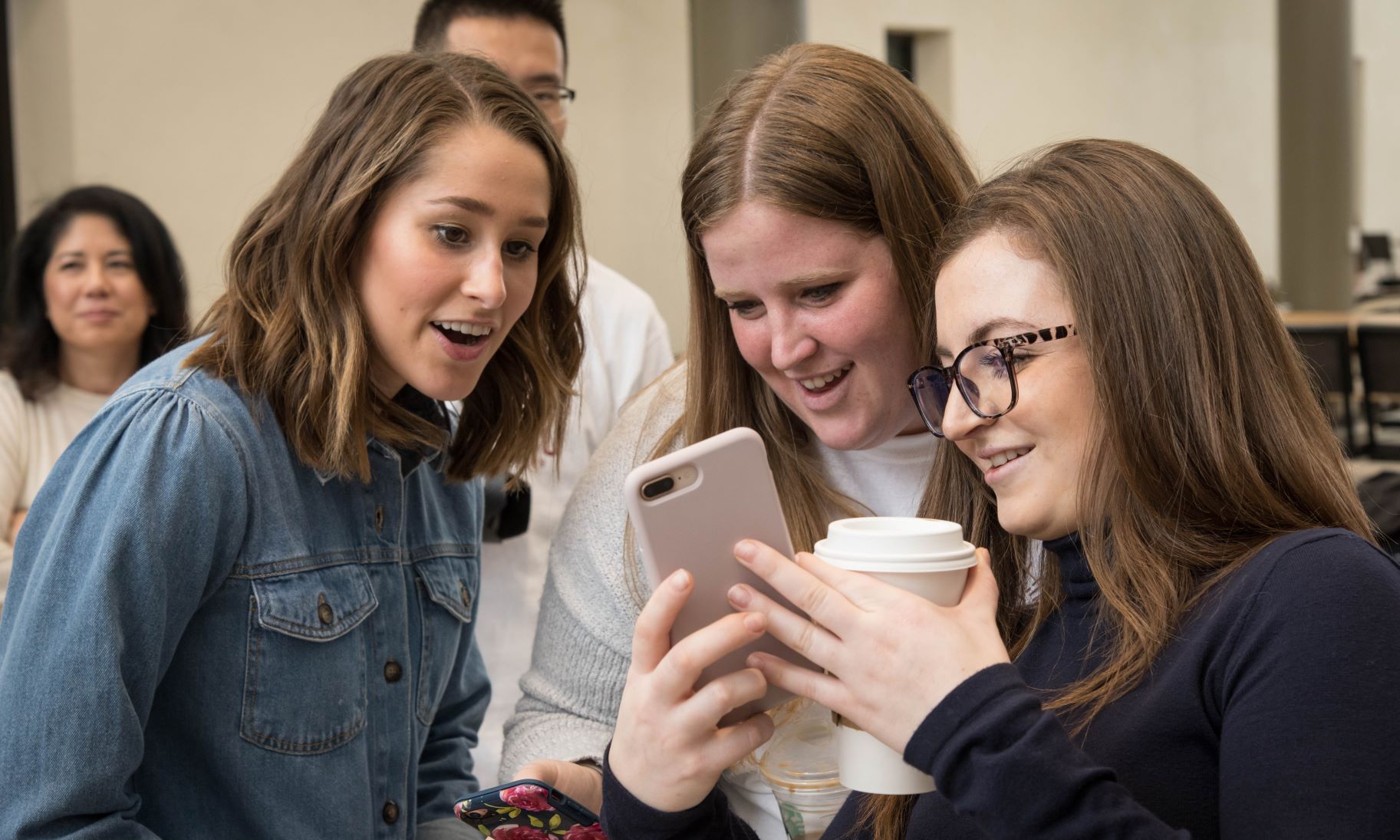 Three people smiling and looking at a smartphone together.