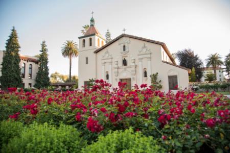 A historic mission church with blooming flowers in the foreground.